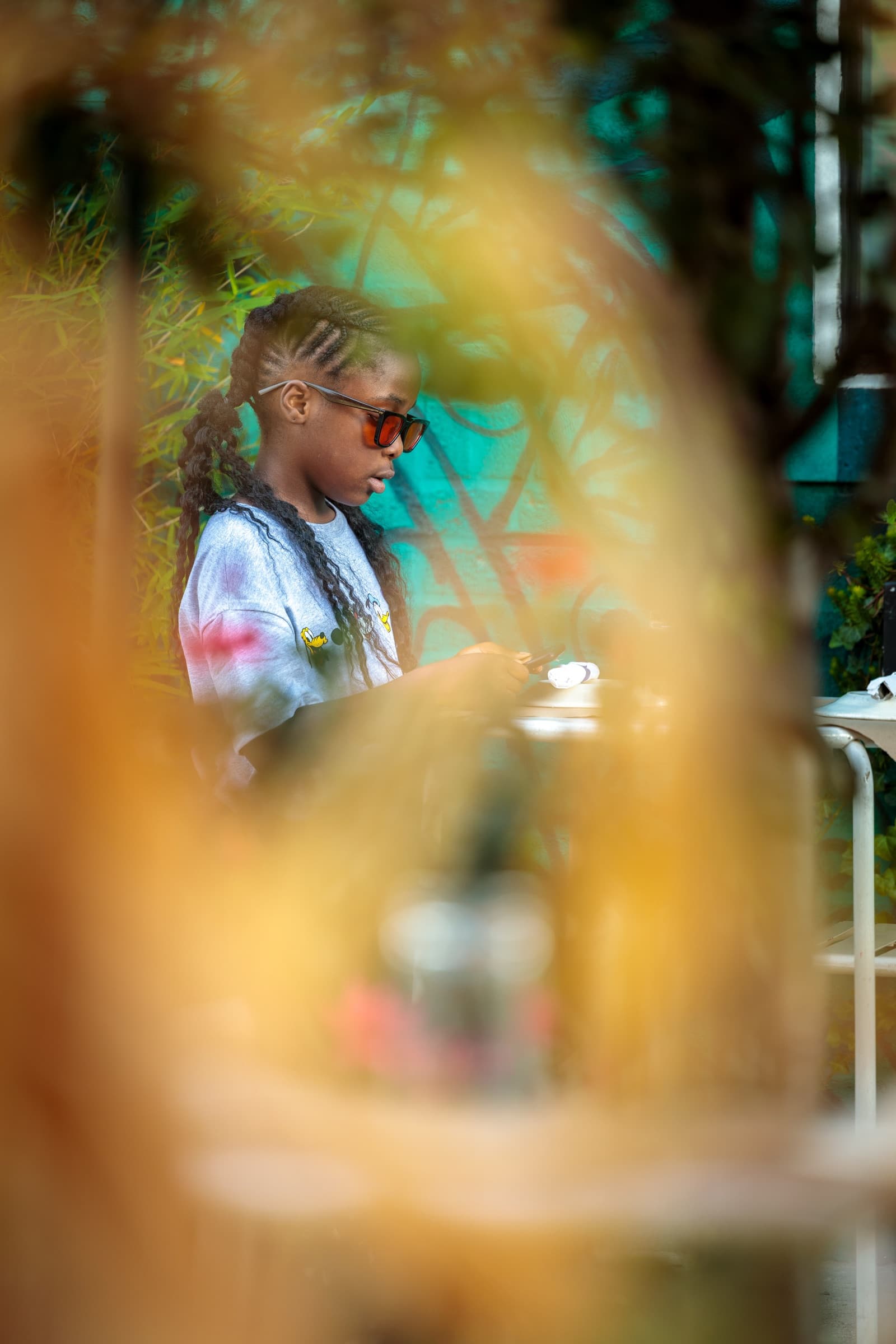 Child seen at a café table through a soft orange out-of-focus foreground of gate and foliage