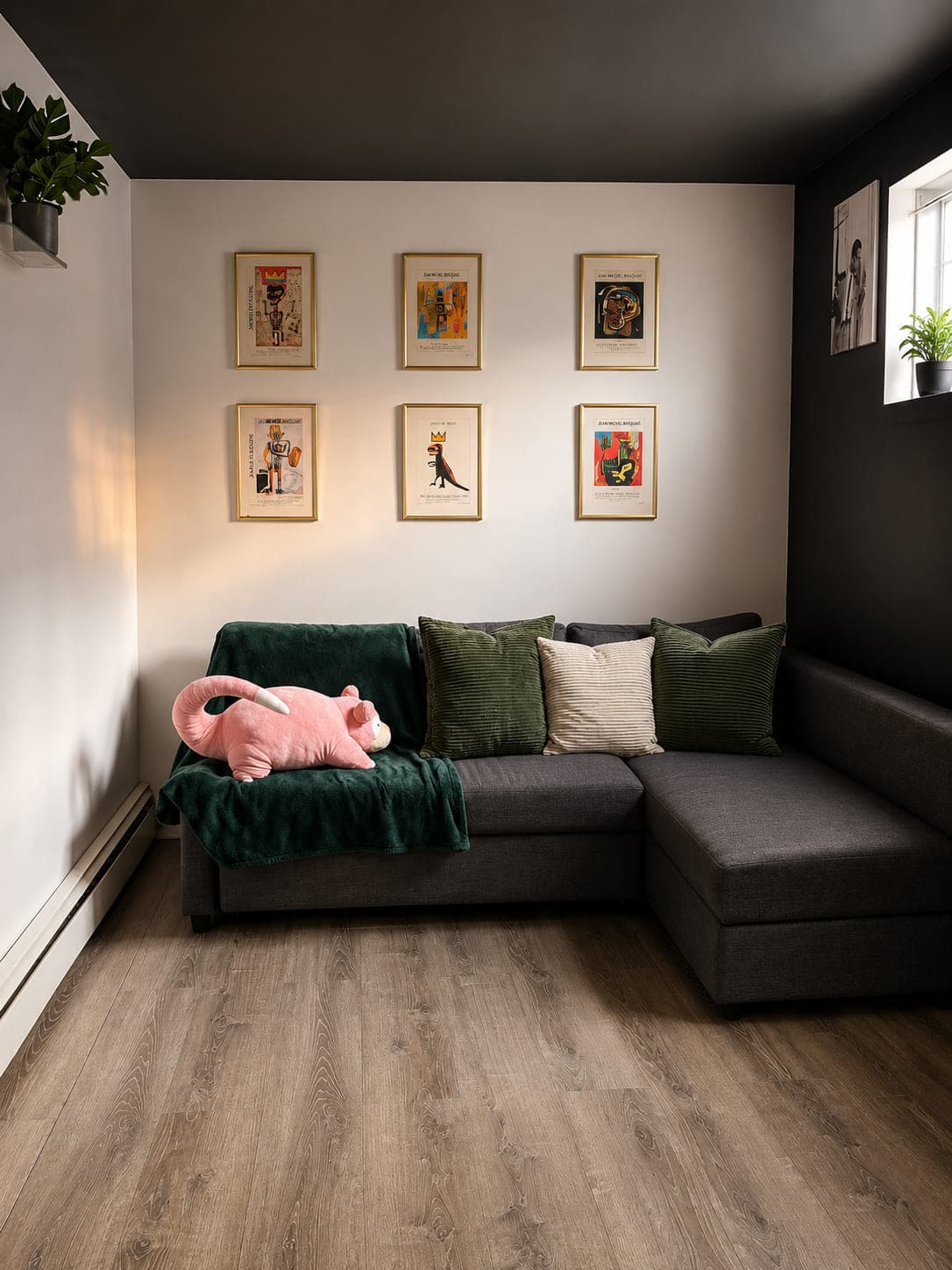 Corner sofa with green throw and pillows beneath a grid of six framed exhibition prints, under a black ceiling
