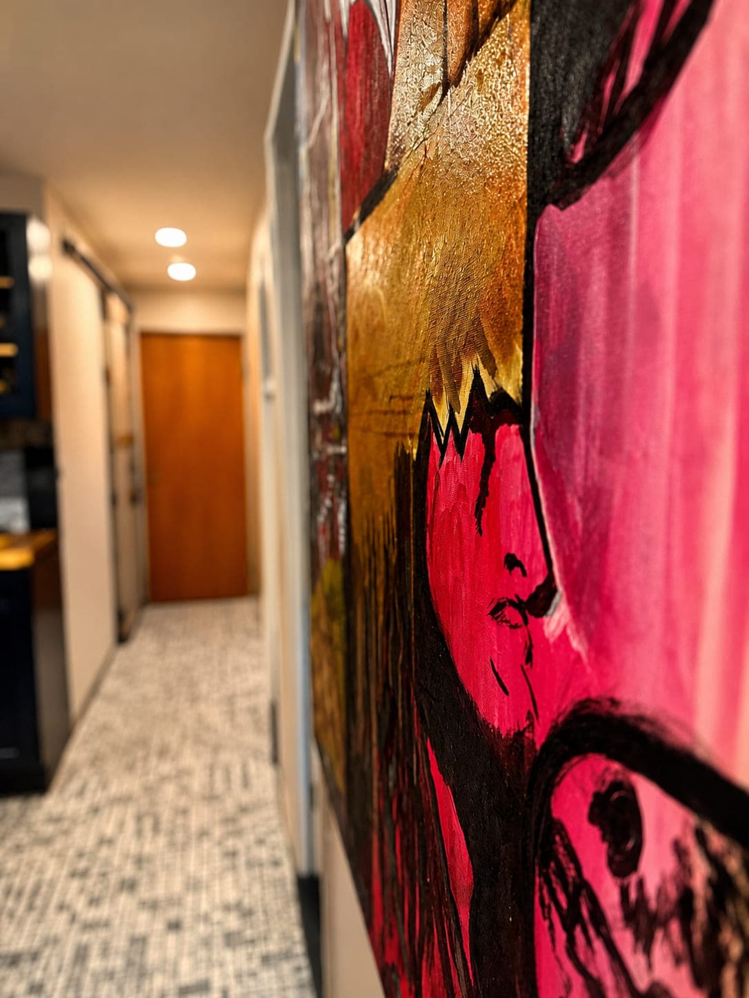 A pink and gold abstract canvas edge-on in the foreground, hallway running back to a wood door