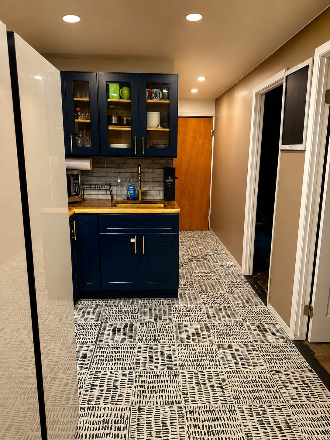 Navy kitchenette with glass-front upper cabinets, butcher-block counter, brass tap and patterned tile floor