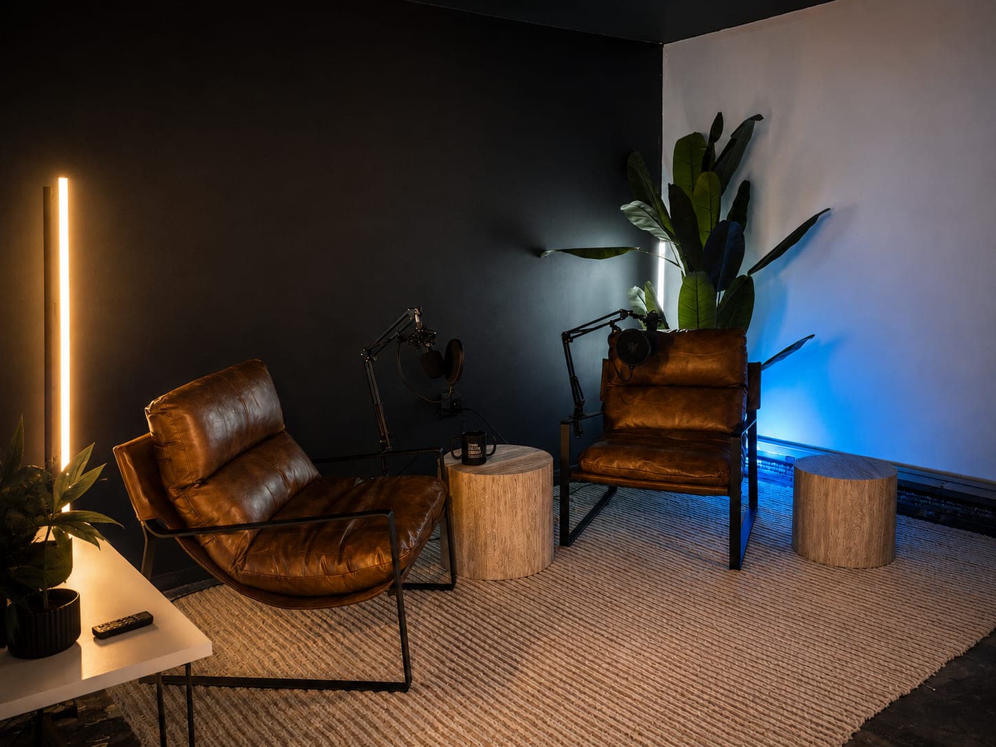 Leather lounge chairs and plants lit by a warm vertical lamp on one side and a cool blue wash on the other